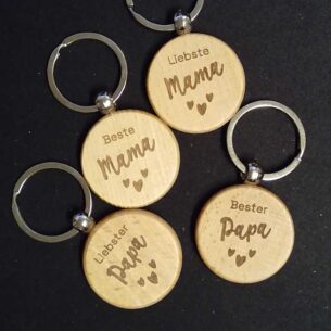 Vier runde Schlüsselanhänger aus hellem Buchenholz mit den Gravuren "Liebste Mama", "Beste Mama", "Liebster Papa" und "Bester Papa" auf dunklem Hintergrund