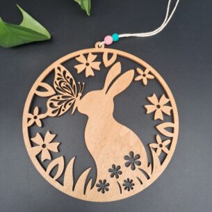 Rundes lasergeschnittenes Holzschild aus Pappel mit einem Hasen, Schmetterling und Blumen, aufgehängt an einer Makramee-Schnur mit zwei Holzperlen