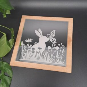 Quadratische Spiegel-Fliese auf Birkensperrholz montiert, mit einer Lasergravur eines Hasen, Schmetterlings und Blumen auf der Glasoberfläche
