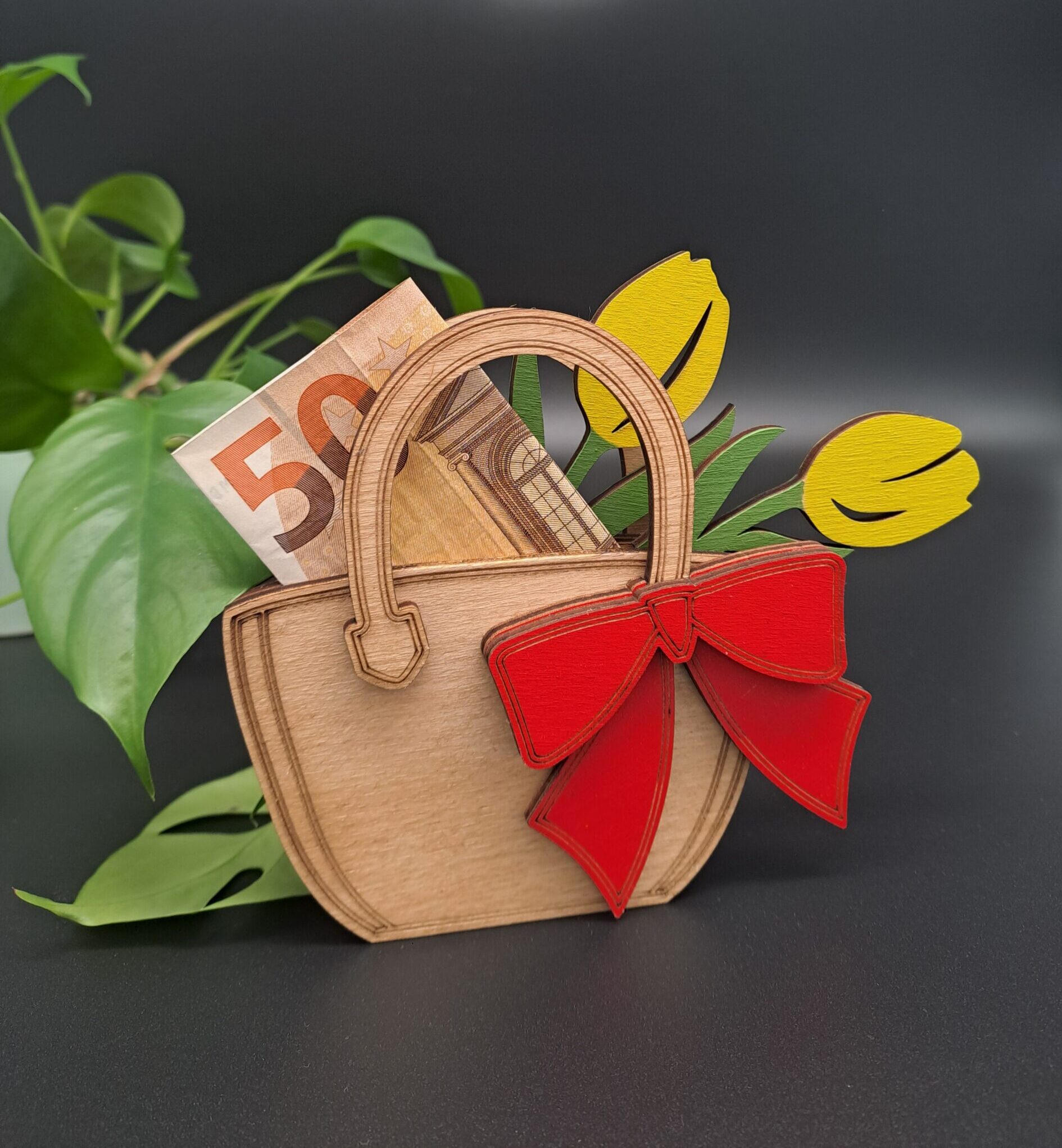 Mehrlagige Holz-Tasche aus Pappel mit gelben Tulpen und einer großen roten Schleife. In der Tasche steckt ein 50-Euro-Schein. Im Hintergrund ist eine grüne Pflanze zu sehen.