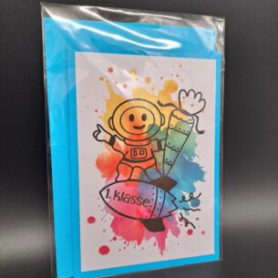 Eine in Cellophan verpackte A6 Klappkarte zur Einschulung mit einem blauen Umschlag im Hintergrund. Das Motiv zeigt einen illustrierten Astronauten auf einer Rakete mit der Aufschrift "1. Klasse" vor bunten Aquarell-Farbspritzern.