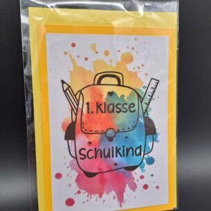 ine Klappkarte zur Einschulung im A6-Format, verpackt in Cellophan mit einem gelben Umschlag. Das Motiv zeigt einen Schulranzen mit Bleistift und Lineal vor bunten Aquarell-Spritzern und den Text "1. Klasse Schulkind"