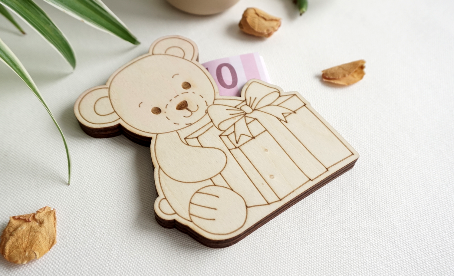 Sitzendes Bärchen mit Geschenk vor sich, aus hellem Holz. Seitlicher Schlitz, zum einstecken von gefalteten Geldscheinen oder Standard Geschenkkarten. dekorative Geschenkidee. Flach, aus drei lagen Holz. kann stehen oder liegen.