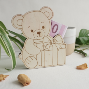 Sitzendes Bärchen mit Geschenk vor sich, aus hellem Holz. Seitlicher Schlitz, zum einstecken von gefalteten Geldscheinen oder Standard Geschenkkarten. dekorative Geschenkidee. Flach, aus drei lagen Holz. kann stehen oder liegen.