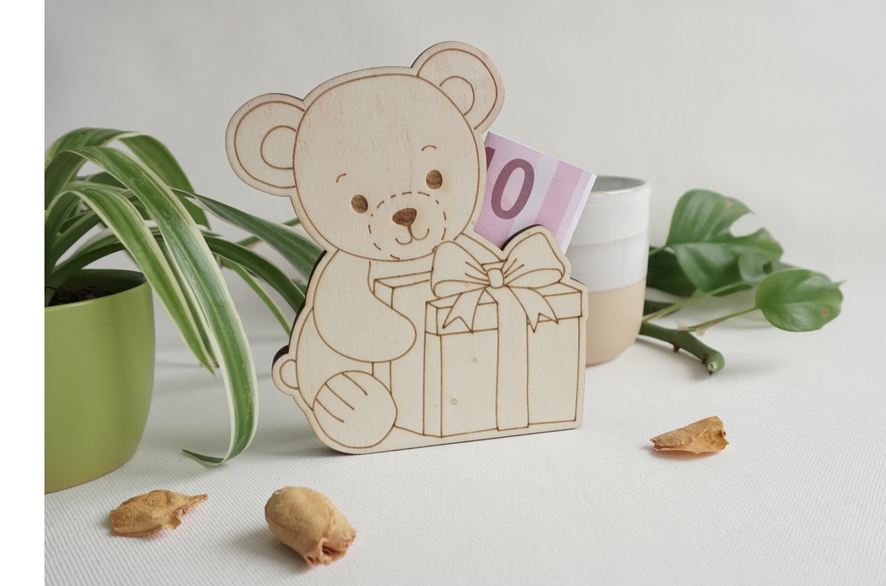 Sitzendes Bärchen mit Geschenk vor sich, aus hellem Holz. Seitlicher Schlitz, zum einstecken von gefalteten Geldscheinen oder Standard Geschenkkarten. dekorative Geschenkidee. Flach, aus drei lagen Holz. kann stehen oder liegen.